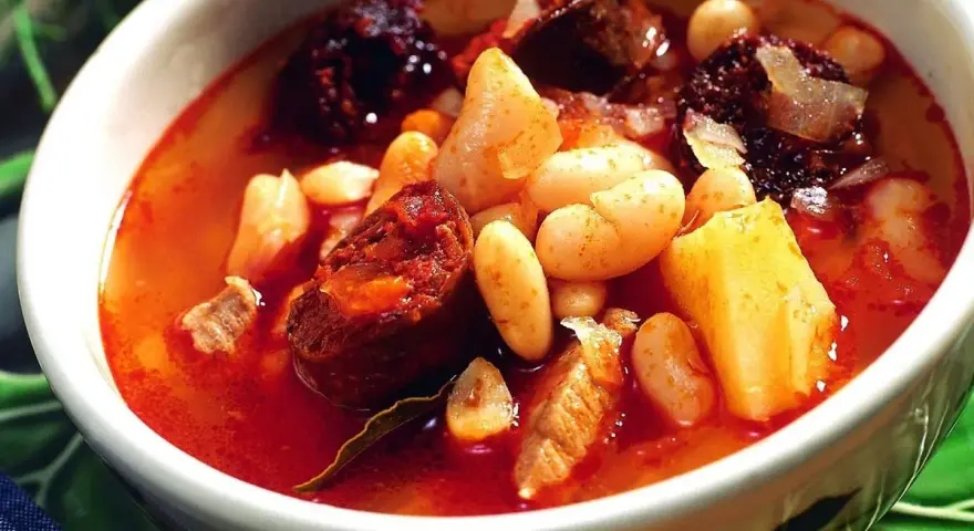 Un reconfortante plato de alubias con chorizo, trozos de morcilla y patatas en un caldo rojizo.