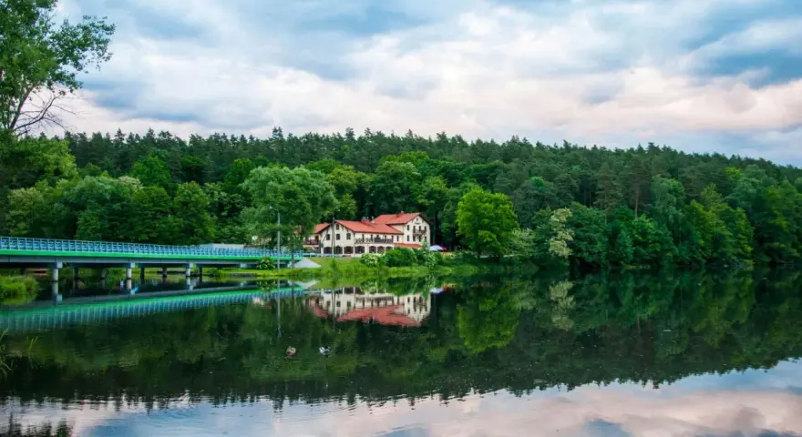 Malowniczy hotel nad jeziorem, z mostem i lasem w tle. Idealne miejsce na wypoczynek i odkrywanie tleń atrakcji.