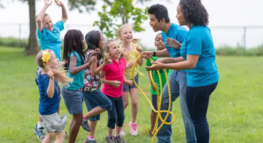 Des enfants et des animateurs jouent à la corde à sauter dans un parc.
