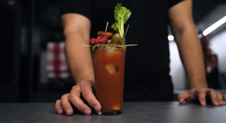 Bloody Mary na soku pomidorowym kontra na passacie. W szklance drink z lodem, ozdobiony oliwkami, suszonym pomidorem, kiełbaską i selerem.