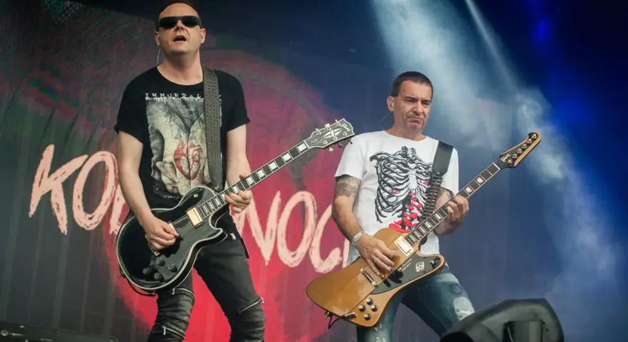 Dwóch gitarzystów na scenie, jeden w czarnej koszulce z sercem, drugi w białej z żebrami. Kocham cię jak Irlandię, grają rocka.