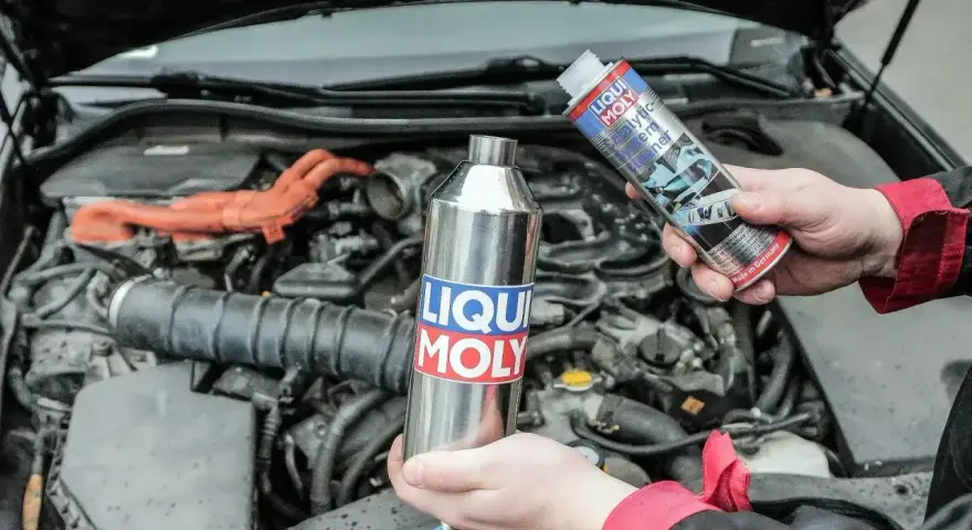 Dwie ręce trzymają produkty Liqui Moly, jeden metalowy, drugi w sprayu, gotowe do czyszczenia katalizatora w silniku samochodu.