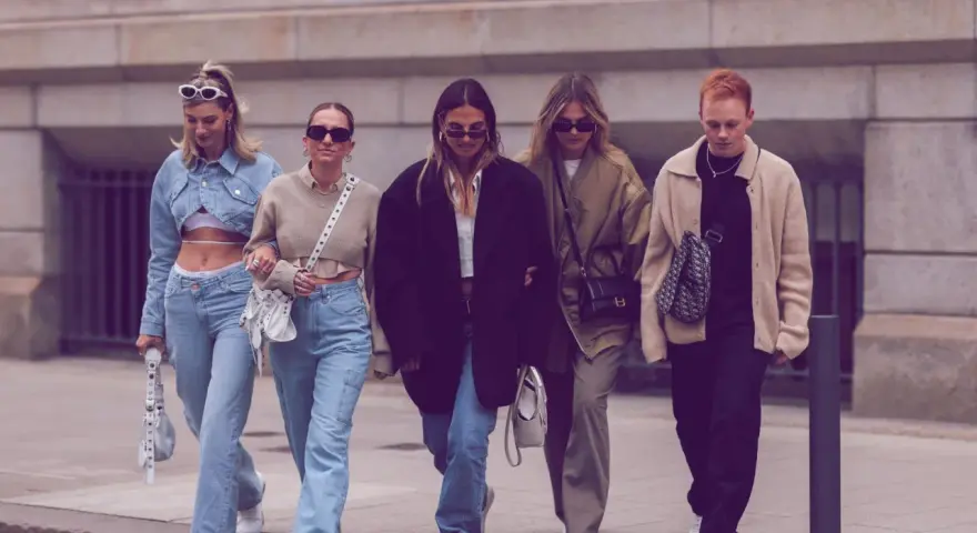 Fünf Freunde spazieren lässig, alle tragen Jeans. Welche Jeans sind in? Weite Schnitte und helle Waschungen dominieren den Look.
