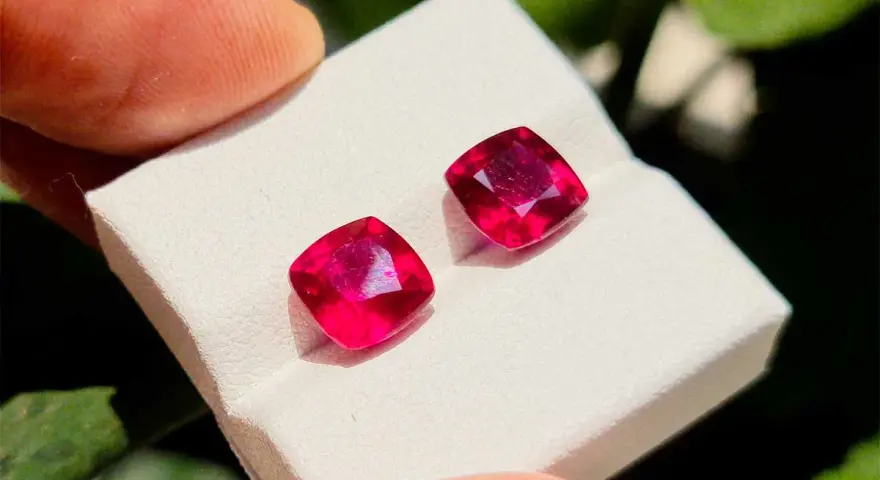 Due gemme rosse intense, la pietra di luglio per eccellenza, brillano su un supporto bianco.
