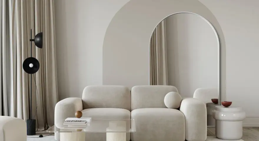 Nowoczesny salon z beżową kanapą, łukiem nad lustrem i stolikiem kawowym. Inspiracja, jak zrobić łuk w aranżacji wnętrz.