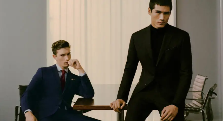 Dos hombres con trajes elegantes, uno azul y otro negro, demuestran el estilo business casual en una oficina moderna.