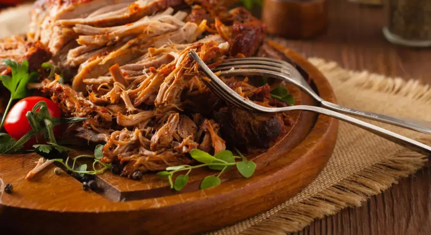 Saftiges Pulled Pork, perfekt zubereitet mit einem aromatischen pulled pork rub, liegt auf einem Holzbrett. Gabeln deuten auf den Genuss hin.