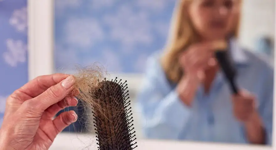 Frauen mit Haarausfall halten eine Bürste mit vielen Haaren. Im Spiegel sieht man eine Frau, die sich die Haare kämmt.