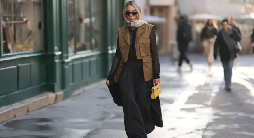 Mujer con chaleco negro corto, falda larga negra y bolso amarillo.