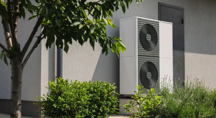 Nowoczesna pompa ciepła 3 5 kw, dyskretnie umieszczona przy ścianie domu, otoczona zielenią, zapewnia ekologiczne ogrzewanie.