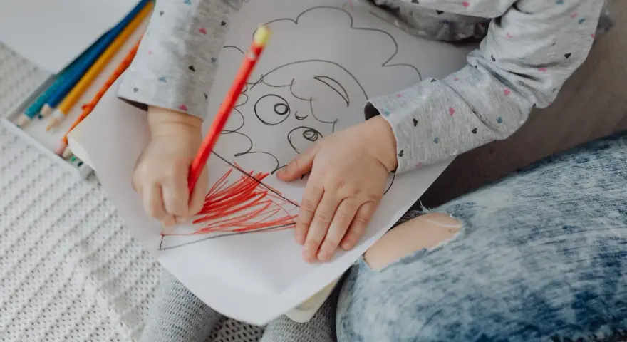Mały rysunek dziecka z kredkami. Dziecko koloruje czerwoną kredką.