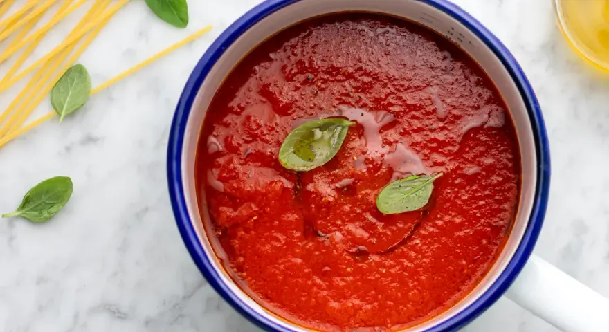 Sugo con pomodorini freschi, basilico e spaghetti crudi su marmo.