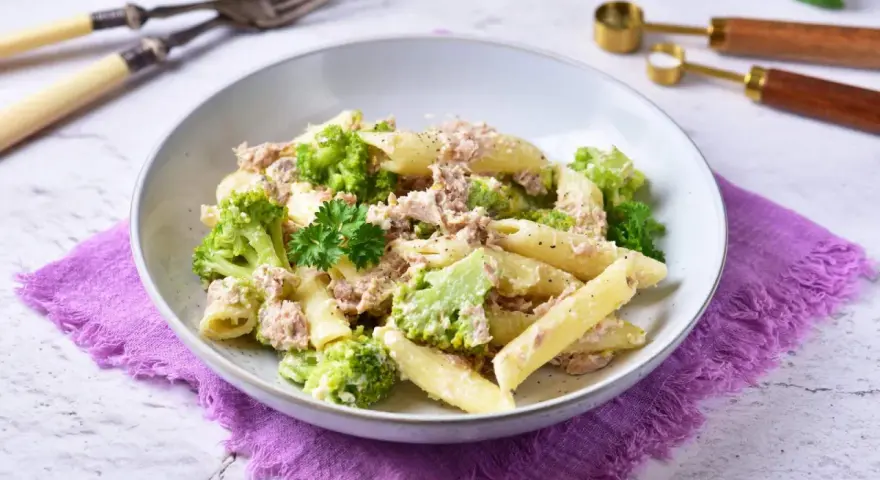 Penne z tuńczykiem i brokułami w kremowym sosie śmietanowo-serowym, udekorowane natką pietruszki.