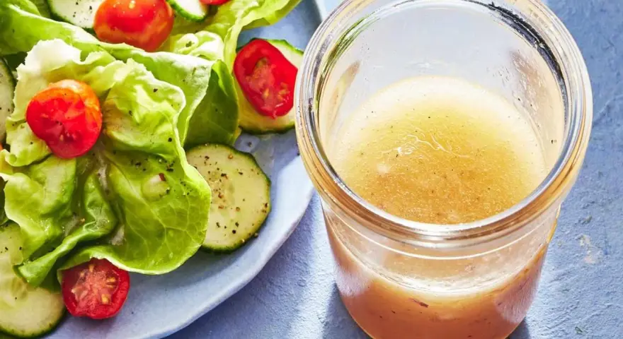 En burk med gyllene dressing till sallad står bredvid en fräsch sallad med sallad, gurka och tomater.