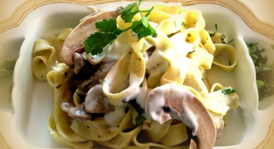Pyszne tagliatelle z grzybami w kremowym sosie, udekorowane natką pietruszki.