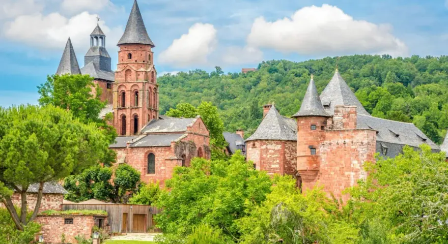 Magnifique ensemble de bâtiments en pierre rouge, dont une église romane et des tours, au milieu d'une végétation luxuriante. Idéal pour découvrir que faire autour de Rocamadour.