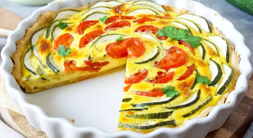 Eine köstliche Zucchini-Quiche mit Tomaten und frischer Petersilie, in einer weißen Quicheform serviert.
