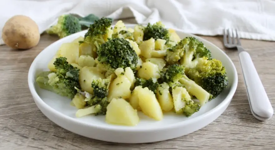Un plato de brócoli con patatas, sencillo y saludable. Una patata entera y trozos de brócoli reposan cerca.