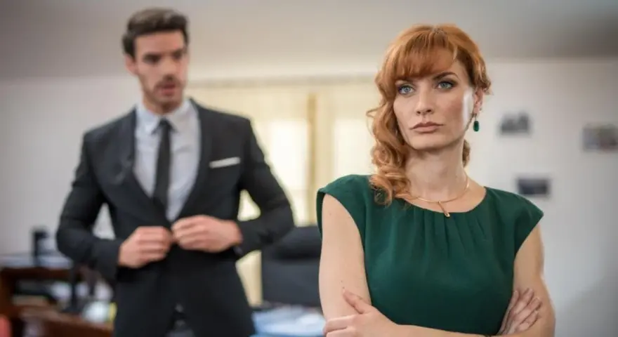 Donna con sguardo preoccupato, mentre un collega in primo piano si sistema la giacca, come se volesse metterla in cattiva luce.