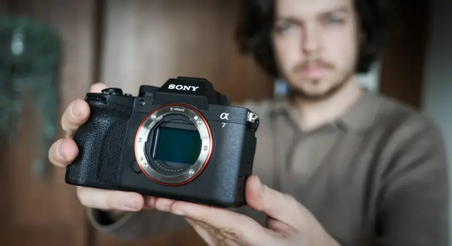 Mężczyzna trzyma aparat Sony Alpha z widocznym obiektywem i mocowaniem E-mount.