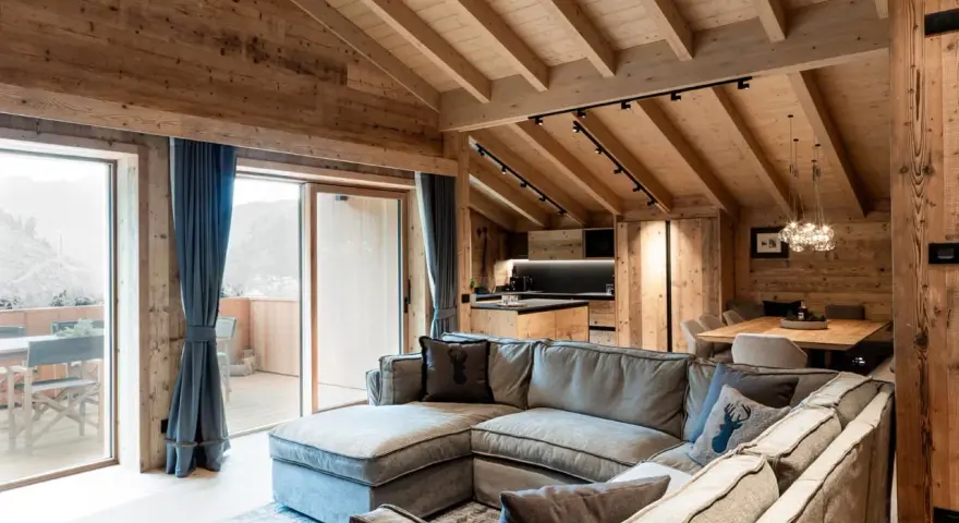 Cozy mountain chalet living room with sectional sofa, wooden beams, and large windows.