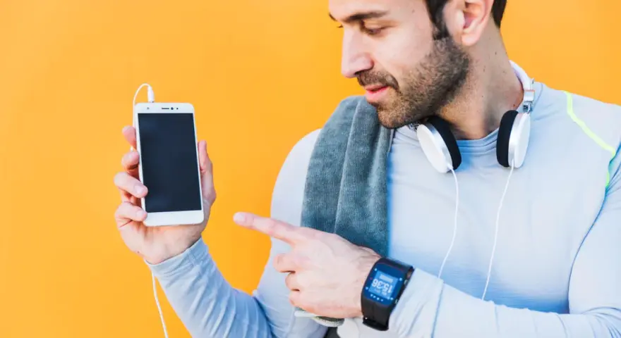 Mężczyzna w sportowym ubraniu pokazuje telefon, jak sparować zegarek z telefonem. Na nadgarstku ma smartwatch.