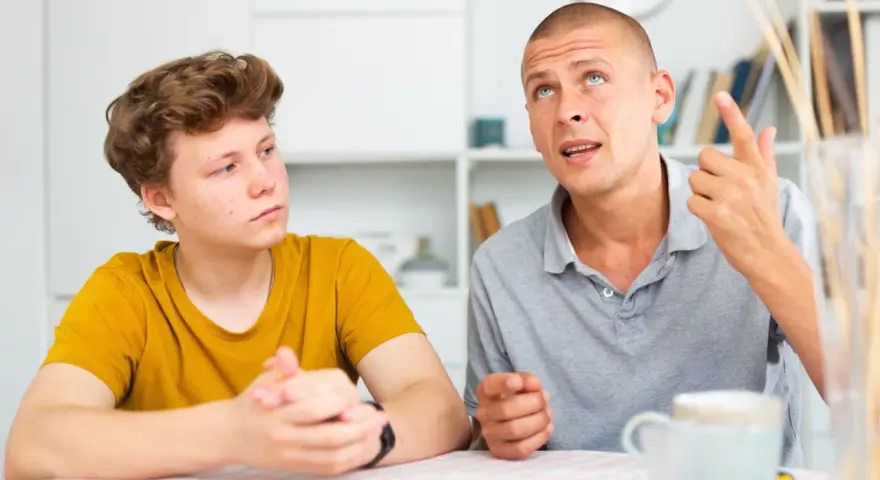 Ojciec tłumaczy synowi, jak rozmawiać z nastolatkiem. Chłopak słucha uważnie, a mężczyzna gestykuluje, podkreślając swoje słowa.