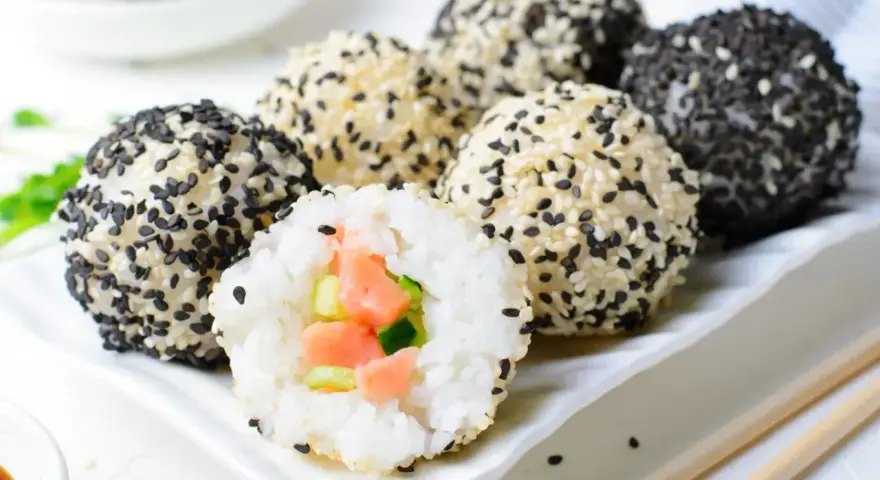 Kuliste sushi, obtoczone białym i czarnym sezamem, z widocznym wnętrzem z łososiem i ogórkiem. Prawdziwa uczta dla miłośników kuchni japońskiej.