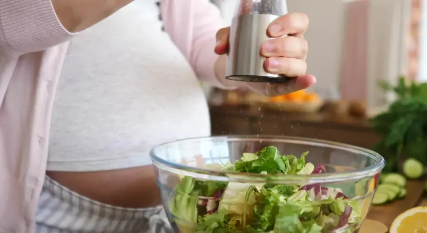 Donna incinta condisce un'insalata fresca. Ricorda come lavare frutta e verdura in gravidanza per una dieta sana.