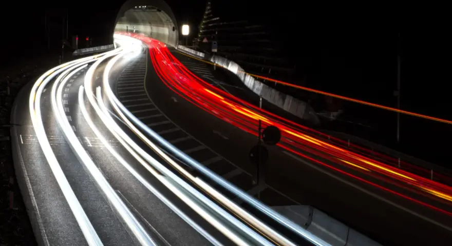 Voiture traversant un tunnel la nuit, capturant les traînées lumineuses des phares et des feux arrière grâce à des photos pose longue.