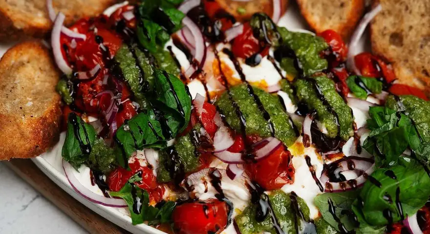 En krämig burrata med tomater, rödlök, basilika och pesto. Perfekt tillbehör till grillat bröd. Ett enkelt burrata recept.