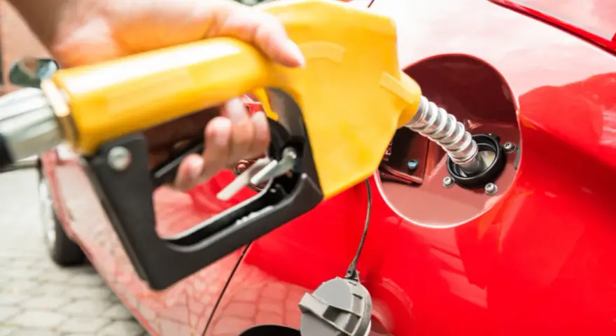 En hand håller en gul pump för att tanka en röd bil. Undrar du vad kostar diesel i Norge?