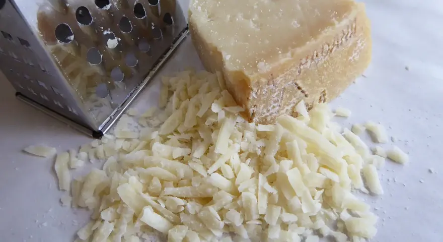 Tarty kawałek parmezanu i świeżo starty ser obok tarki. Dowiedz się, jak przechowywać parmezan, by zachował świeżość.