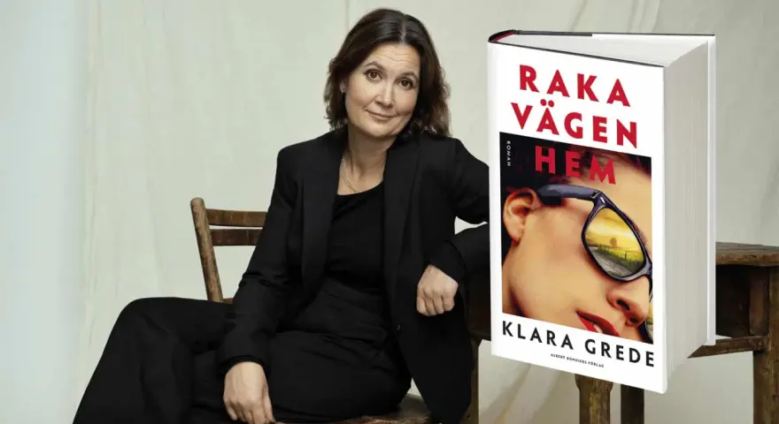 Klara Grede, författaren till "Raka vägen hem", sitter i en stol bredvid sin bok.