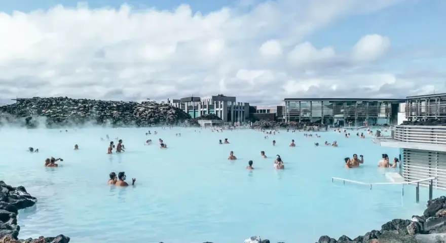Ludzie kąpią się w turkusowej wodzie geotermalnej Blue Lagoon, otoczonej wulkanicznymi skałami i nowoczesnymi budynkami.