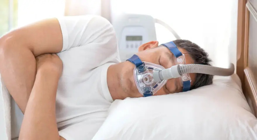Mężczyzna śpi z maską CPAP, która pomaga mu oddychać podczas bezdechu sennego.