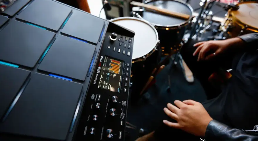 Nowoczesny sampler perkusyjny Roland SPD-SX PRO gotowy do tworzenia rytmów. W tle widoczne elementy zestawu perkusyjnego.