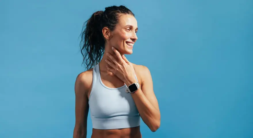 Donna sorridente con orologio sportivo, tocca il collo. Nonostante la sensazione di correre con la febbre, il suo sguardo è positivo.
