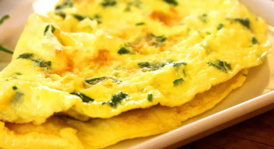 Złożony omlet z zielonymi ziołami na białym talerzu.