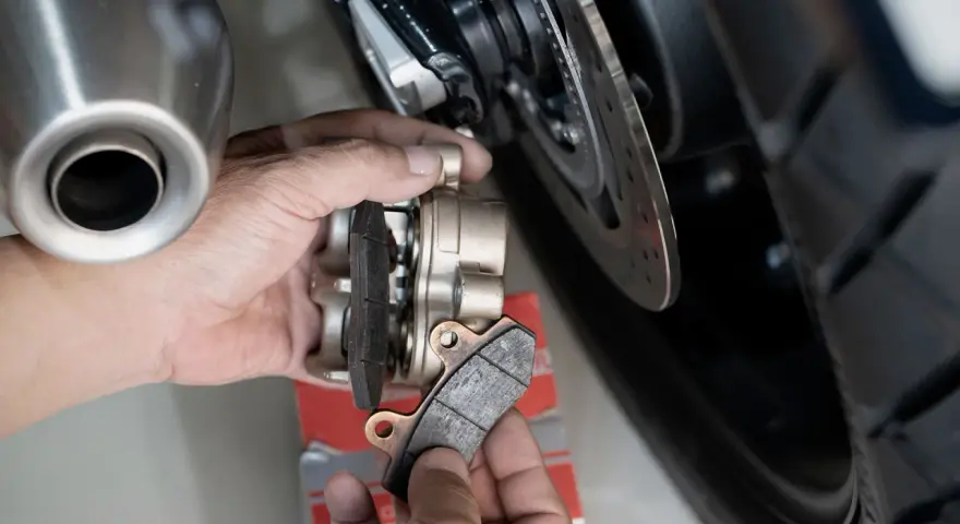 Mani che sostituiscono le pastiglie dei freni anteriori di una moto. Si valuta la durata pastiglie freni anteriori osservando l'usura.