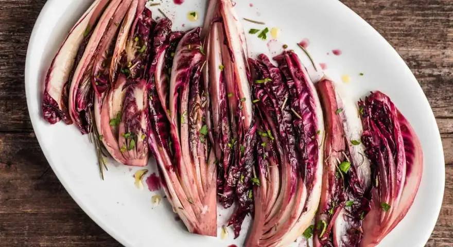 Radicchio al forno, tagliato a spicchi e condito con erbe aromatiche, servito su un piatto bianco.