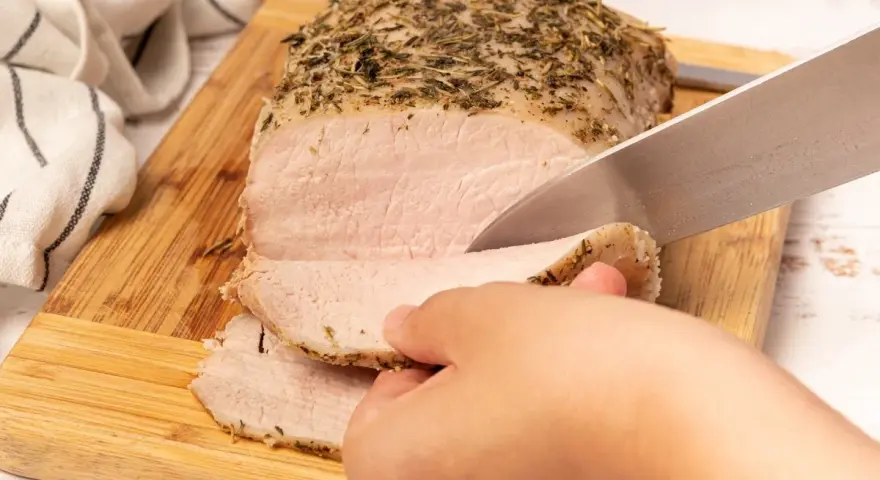 Un jugoso lomo a la sal, cubierto de hierbas, se corta en rodajas tiernas sobre una tabla de madera.