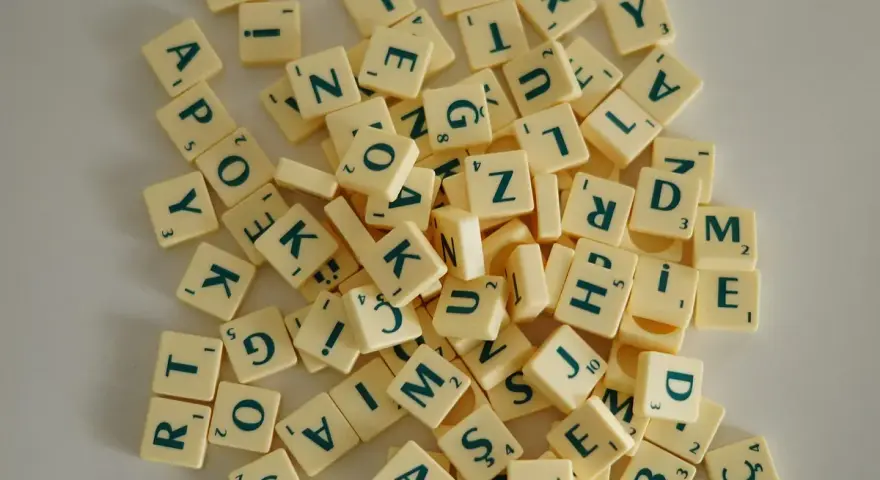Fichas de letras de un juego de mesa, como las del Scrabble, dispersas. Cada ficha tiene una letra y un número. Un ejemplo visual de la diferencia entre lengua e idioma.