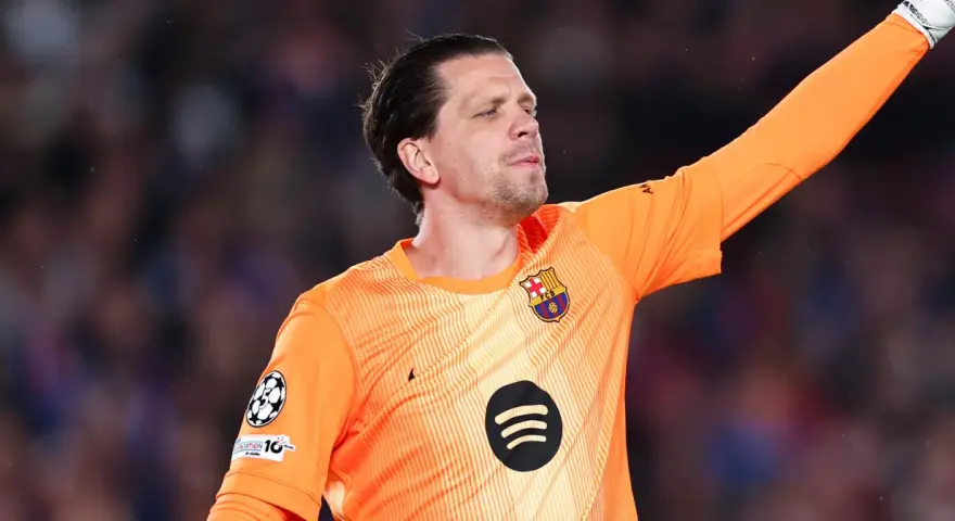 Wojciech Szczęsny w pomarańczowej koszulce bramkarskiej FC Barcelony, z podniesioną ręką, gotowy do obrony.