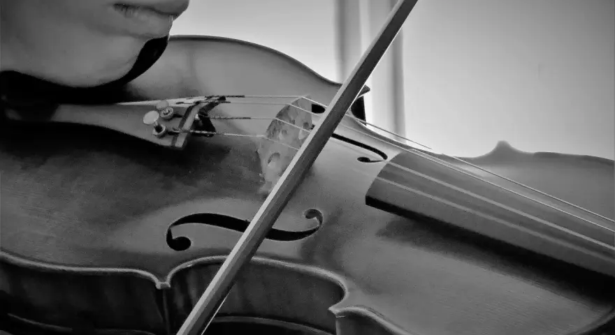 Nahaufnahme einer Person, die eine Geige spielt. Der Bogen streicht über die Saiten und erzeugt die Klänge bester klassischer Musik.
