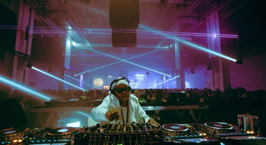 Un DJ année 2000, lunettes de soleil et bandeau, mixe sous des lasers bleus et violets devant une foule en délire.