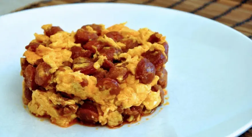 Deliciosa porción de duelos y quebrantos receta, con huevo revuelto y trozos de chorizo, servida en plato blanco.
