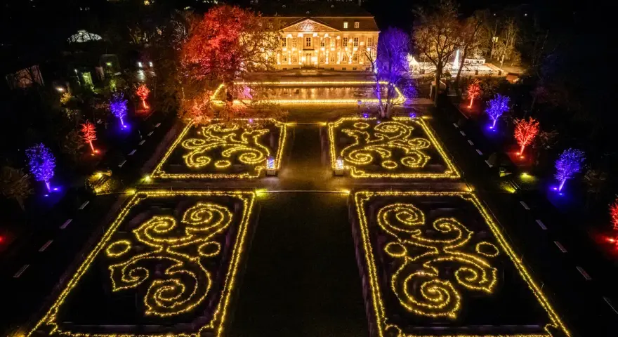 Magische Lichtershow im Tierpark Berlin: Verzauberte Gärten mit leuchtenden Mustern und farbig beleuchteten Bäumen vor einem prachtvollen Gebäude.