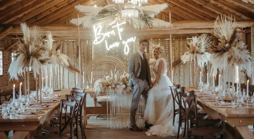 Elegancka sala weselna stodoła z parą młodą, neonem "Born to love you" i boho dekoracjami z traw pampasowych.