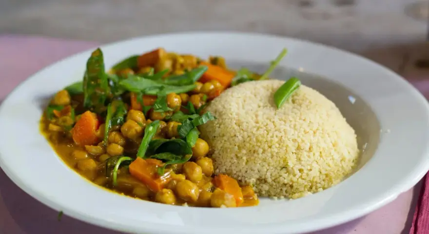 Un plato de cuscus con verduras, garbanzos y zanahoria en una salsa dorada, decorado con hojas verdes.